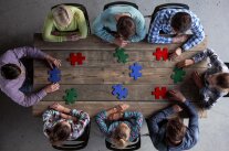 Personen mit großen Puzzleteilen am Tisch von oben