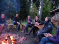 Leute sitzen ums Lagerfeuer, eine junge Frau spielt Gitarre