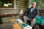 Mann sitzt auf einer Bank vor der Hütte mit Bestimmungsbüchern zu Insekten, Pflanzen, Pilzen.