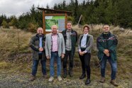 Fünf Personen stehen vor dem Schild des Klimawald-Arboretums Tettau.