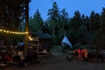 Pulswinkelhütte, Lagerfeuerstelle und Märchenzelt mit vielen Gästen in der Dämmerung