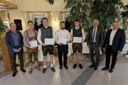 Sieben Männer stehen nebeinander und blicken in die Kamera