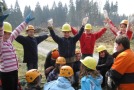 Kinder mit Helmen und einem Forstwirtschaftsmeister stehen eng beieinander und spielen das Durchforstungsspiel