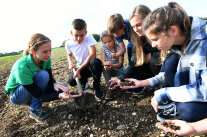 5 Kinder und eine Landwirtin begutachten Ackerboden mit den Händen